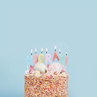 Hooray! taartkaarsen in een regenboog spikkeltaart voor een lichtblauwe achtergrond