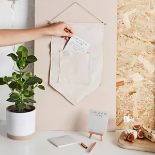 Stoffen doek met zakje wordt gevuld met kaartjes en staat naast een groene plant in een witte pot