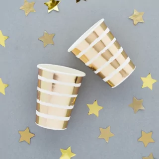 bekers met witte en gouden strepen liggen op een grijze achtergrond naast sterretjes confetti