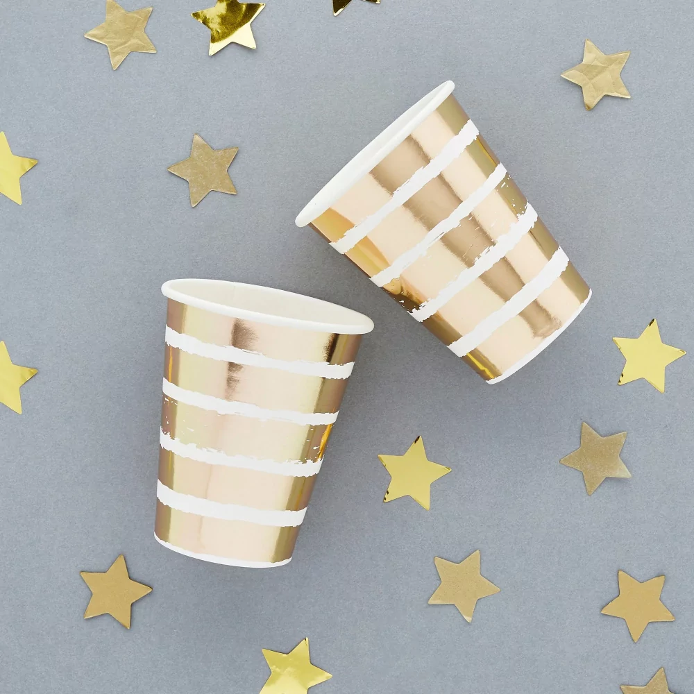 bekers met witte en gouden strepen liggen op een grijze achtergrond naast sterretjes confetti