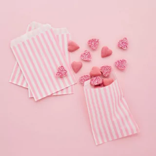roze achtergrond met roze en wit gestreepte zakjes gevuld met snoep hartjes