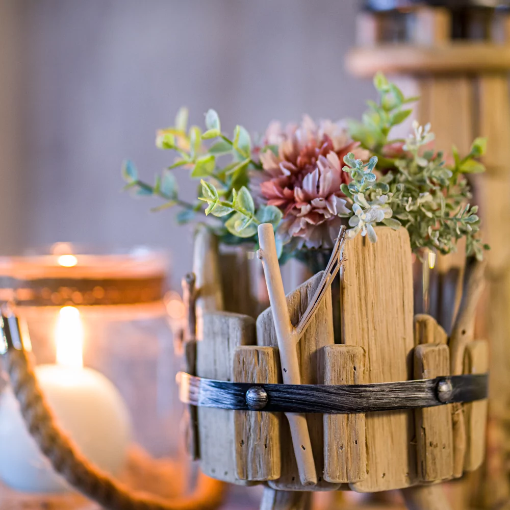 Houten bakje gevuld met droogbloemen en nepbloemen staat voor een ronde witte kaars in een glazen pot