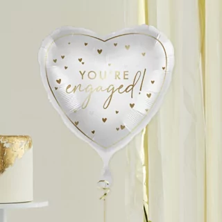 hartvormige folieballon in het wit met gouden tekst you're engaged en gouden hartjes zweeft voor een goud met witte taart