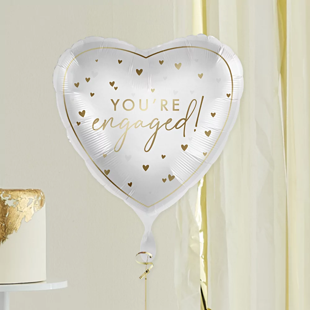 hartvormige folieballon in het wit met gouden tekst you're engaged en gouden hartjes zweeft voor een goud met witte taart