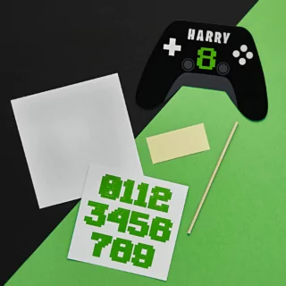 personaliseerbare taart topper in de vorm van een zwarte controller met stickervellen in het groen en wit op een zwart met groene achtergrond