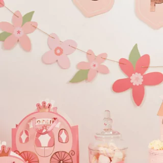 Roze bloemenslinger hangt aan een beige muur achtern een cadeautasje in de vorm van een koets en een glazen pot met spekjes