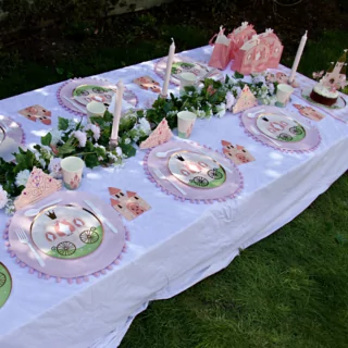 Tafel versierd met een roze tiara, bordjes met een koets erop en cadeautasjes in de vorm van een koets naast een bloemenslinger en een lange kaars