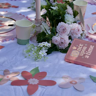 Tafel versierd met een roze tiara, bordjes met een koets erop en cadeautasjes in de vorm van een koets naast een bloemenslinger en een lange kaars