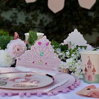 Tafel versierd met een roze tiara, bordjes met een koets erop en cadeautasjes in de vorm van een koets naast een bloemenslinger en een lange kaars