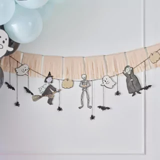 Oranje tasselslinger met spookfiguurtjes zoals een spookje, heks, vampier en skelet hangt voor een witte muur naast een mint ballonnenboog