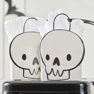 Cadeautasje met een doodshoofd erop in het zwart en wit staat op een zwarte kruk en is gevuld met wit tissuepapier