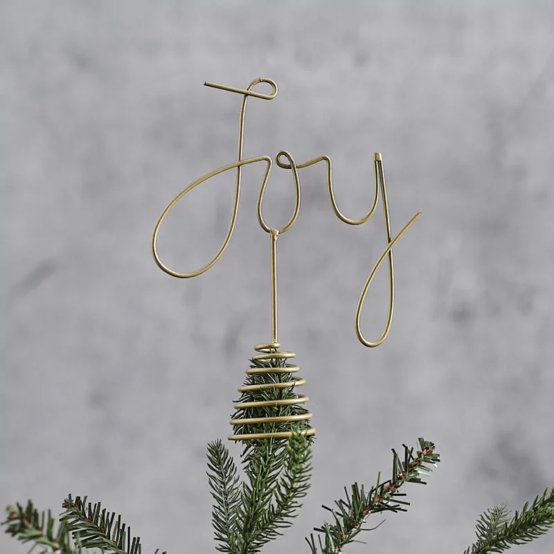 Gouden piek met de tekst joy zit bovenop een groene tak voor een grijze muur