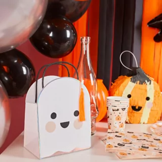 Cadeautas in de vorm van een spookje staat op een tafel versierd met pompoenen confetti en een pinata