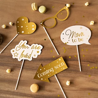 Photobooth props in het goud en nude voor een babyshower liggen op een houten tafel
