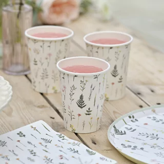 Bekers versierd met bloemen en planten staan op een houten tafel naast bijpassende borden en servetten