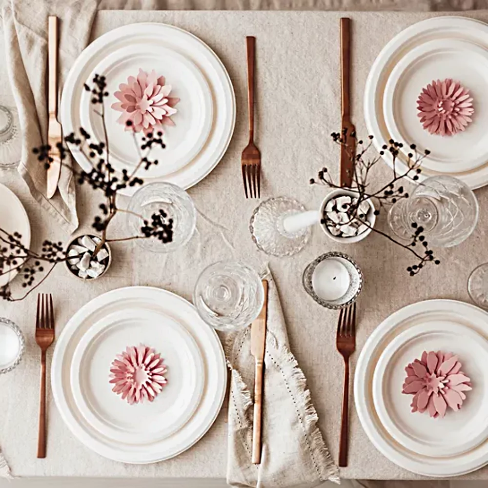 Tafel versierd met goud bestek, witte borden en roze bloemen