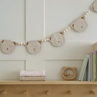 Slinger met houten teddy beren en kralen in het bruin en wit hangt boven een houten kastje aan een witte muur