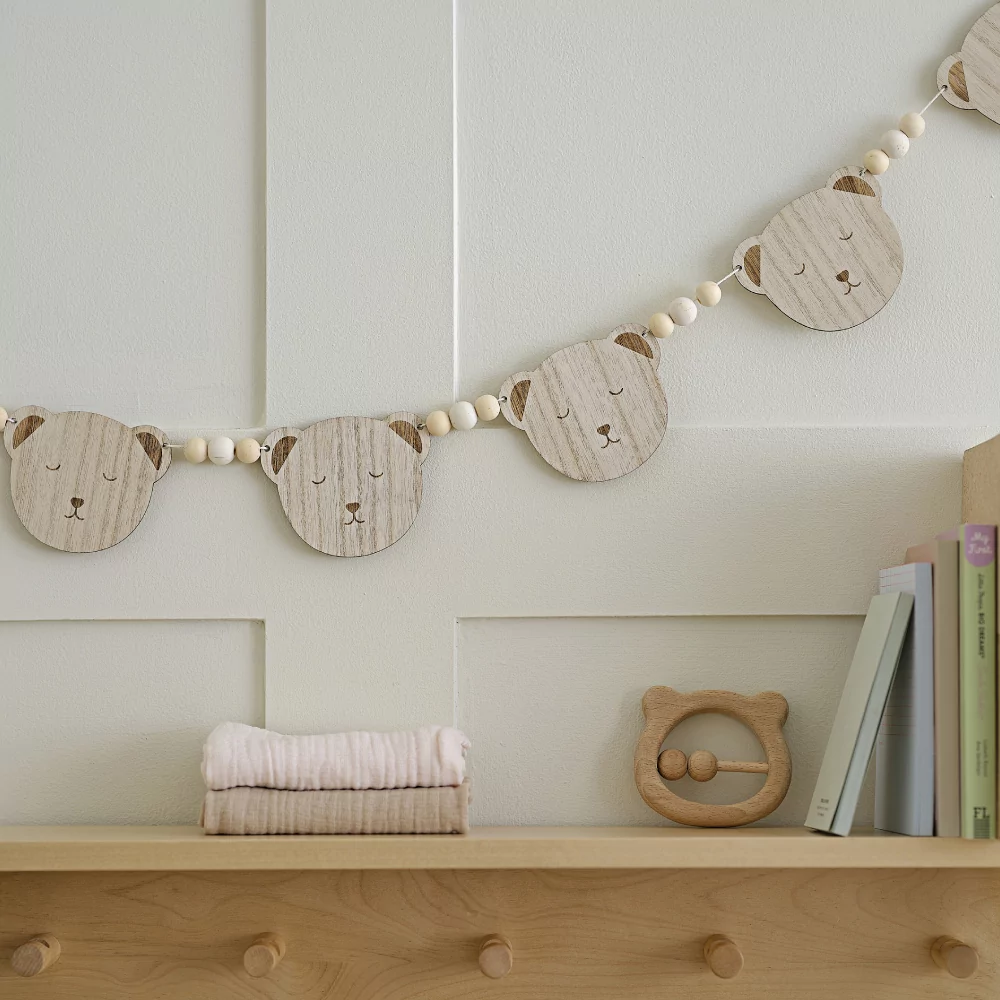 Slinger met houten teddy beren en kralen in het bruin en wit hangt boven een houten kastje aan een witte muur