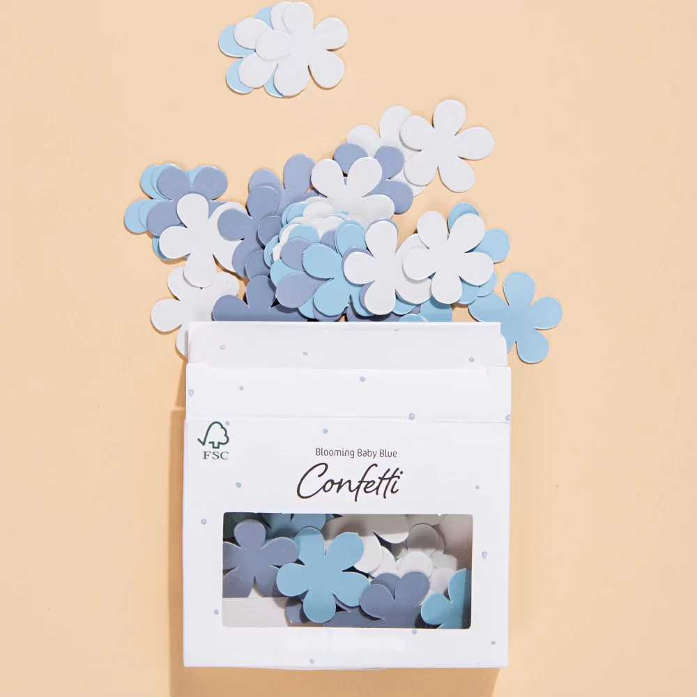 blauwe en witte confetti bloemen liggen op een gele ondergrond en zitten in een wit met blauw doosje
