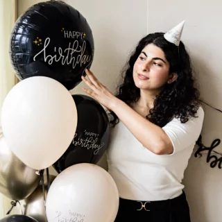 vrouw met zwarte krullen en een tros creme en zwarte ballonnen