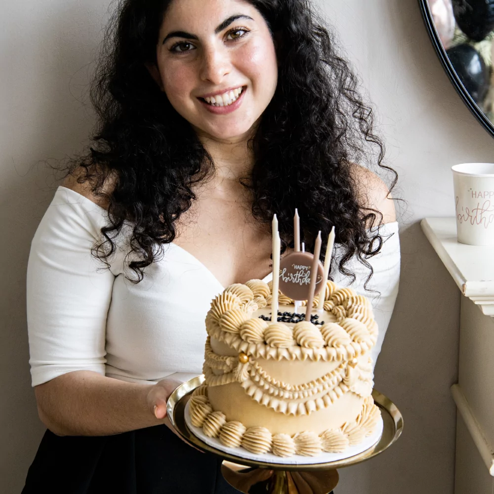 dame met zwarte krullen en een creme kleurige taart met beige en roze kaarsen