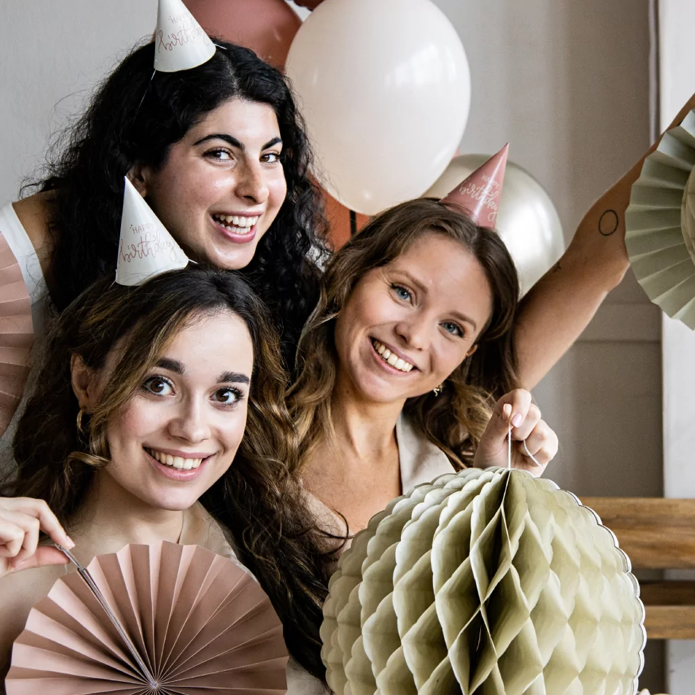 drie vrouwen op een verjaardag met witte en roze feesthoedjes met de tekst happy birthday