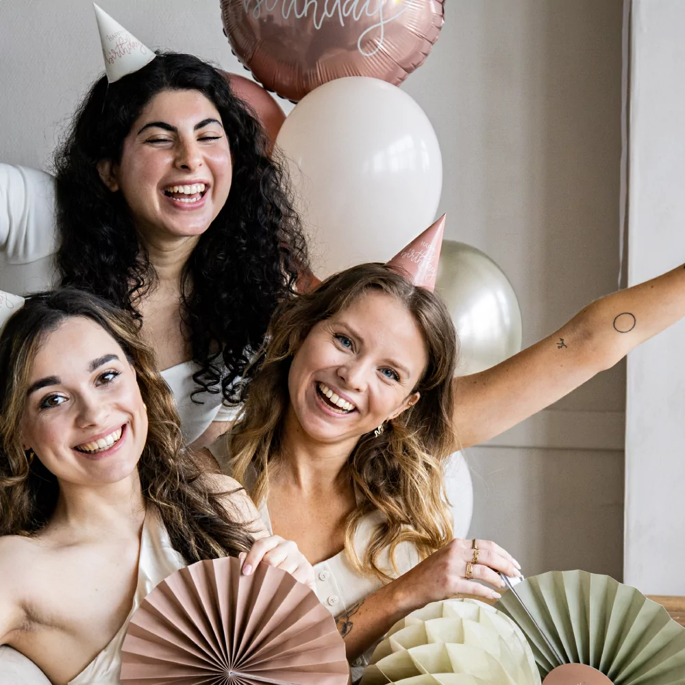 drie vrouwen op een verjaardag met witte en roze feesthoedjes met de tekst happy birthday