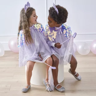 twee meisjes met zeemeermin verkleedkleding en een haarband met schelpen zitten op een witte kruk