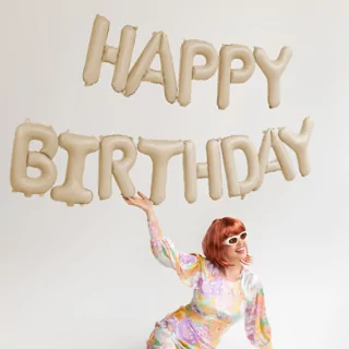 beige ballonnen met de tekst happy birthday hangen boven een vrouw met rood haar