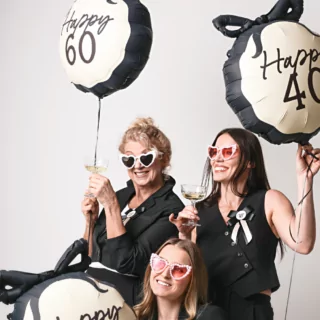 drie vrouwen in zwarte pakken met ballonnen in het creme en zwart met de teksten happy 40 en happy 60