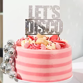 zilveren taart topper met de tekst lets disco zit bovenop een roze taart met fruit en discoballen