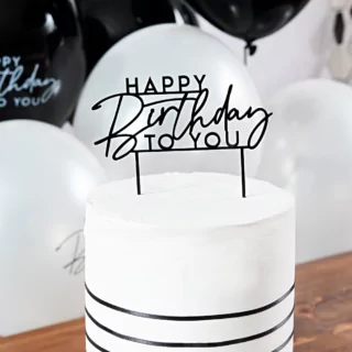 zwarte taartversiering happy birthday to you zit in een wit met zwarte taart en staat op een bruine tafel