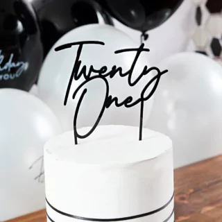 zwarte taartversiering twenty one zit in een witte taart en staat op een bruine tafel